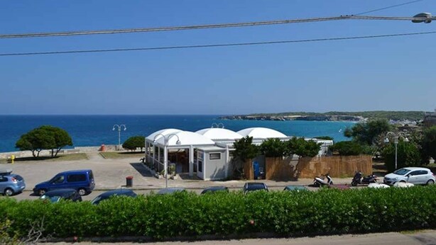 Un hotel frente al mar con estructuras blancas abovedadas, un estacionamiento con coches y vistas al océano.