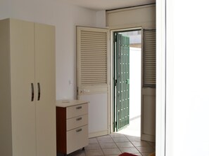 A room with a wardrobe, a small desk, and a door leading outside.