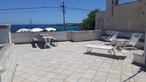 Una terraza en la azotea con suelo de baldosas, una mesa, bancos y dos tumbonas.