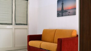 Una habitación con un sofá rojo, una ventana con persianas y un cuadro de un faro en la pared.