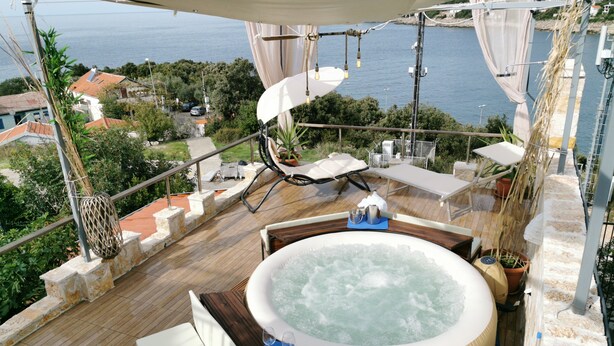 Eine Dachterrasse mit Whirlpool, Liegestühlen und Meerblick.