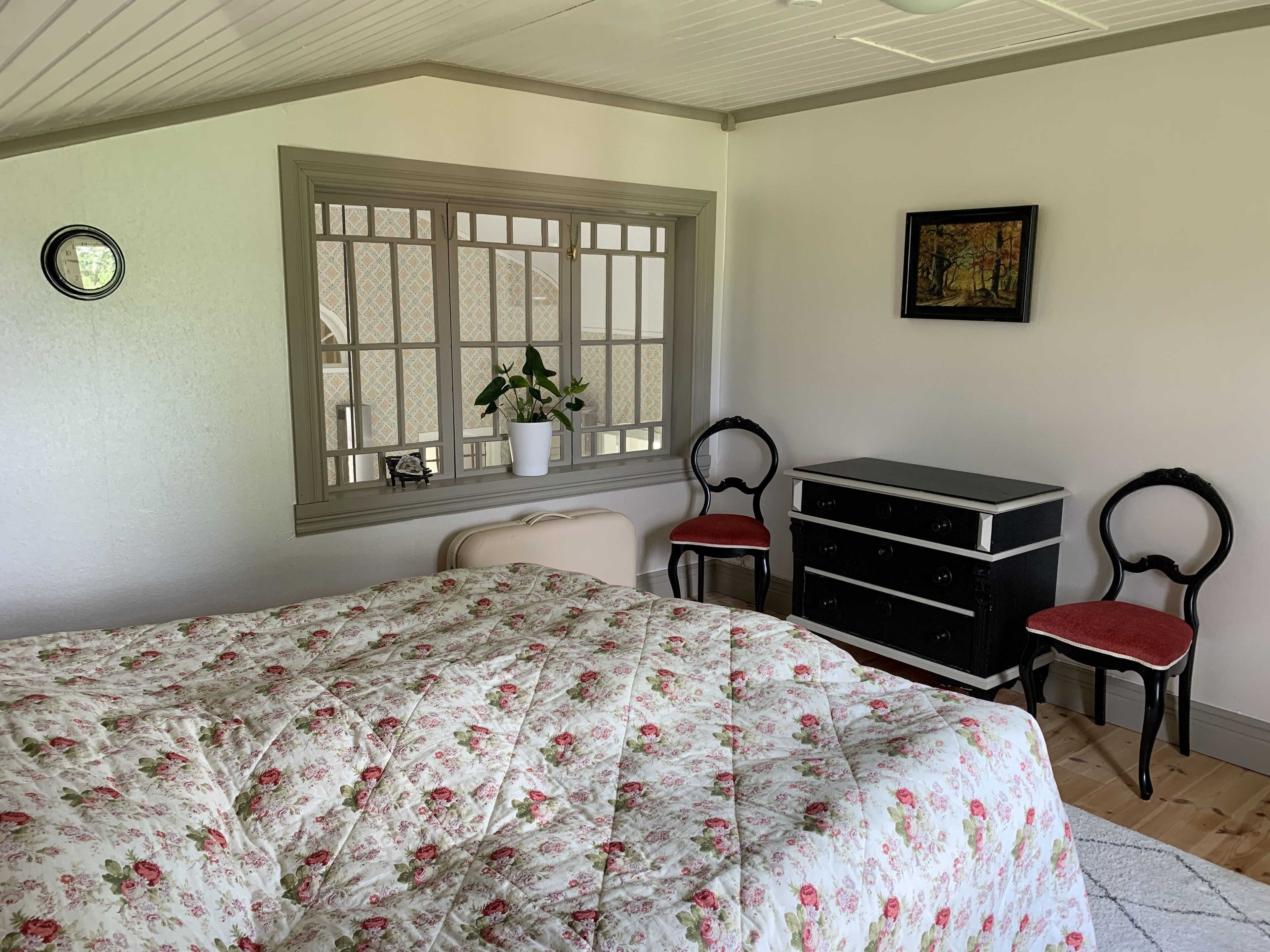 Ein Schlafzimmer mit blumigem Bettbezug, einem Fenster mit Blick, einem Schminktisch und zwei Stühlen.