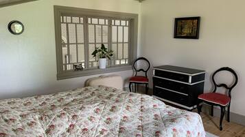 Ein Schlafzimmer mit blumigem Bettbezug, einem Fenster mit Blick, einem Schminktisch und zwei Stühlen.