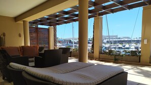 Un espace extérieur aménagé, abrité et doté de mobilier en osier, offrant une vue sur un port de plaisance.