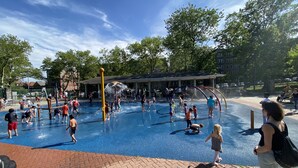 A water play area with multiple slides and water features, surrounded by trees and a covered seating area.