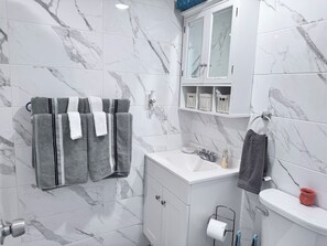 A bathroom with marble tiles, a white sink, a toilet, and a towel rack with multiple towels. - Room-private 2 Bedrooms, new Shower Bath (North Bergen)