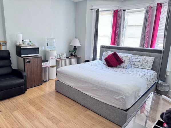 A modern hotel room with a grey bed, a black chair, a minibar, a water dispenser, and a radiator. - Room-private 2 Bedrooms, new Shower Bath (North Bergen)