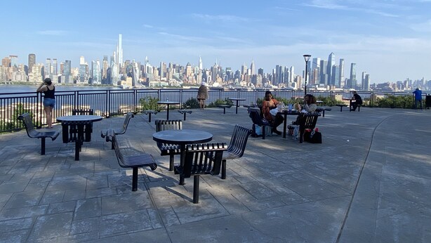 An outdoor seating area with tables and chairs, overlooking a city skyline.
