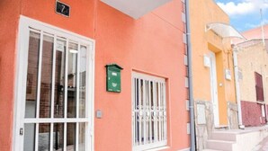 Un bâtiment portant le numéro « 7 », une porte avec des panneaux de verre, une fenêtre avec des barreaux en métal et un escalier menant à une zone abritée.