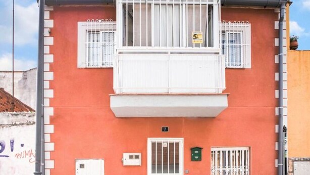 Un bâtiment à deux étages avec une façade rouge, des barreaux blancs aux fenêtres et un petit balcon.