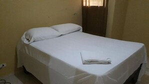Ein Einzelbett mit weißer Bettwäsche in einem Zimmer mit gelben Wänden und einem Vorhang.