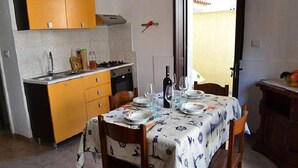 A dining area with a table set for four, a kitchen in the background, and a door leading outside. - Three-room Holiday Home With Outdoor Space and a few Steps From the Cliff (Melendugno)