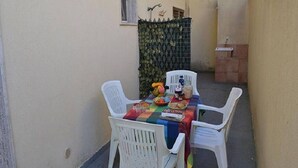 A small outdoor dining area with a table set for two, surrounded by white plastic chairs. - Three-room Holiday Home With Outdoor Space and a few Steps From the Cliff (Melendugno)