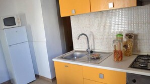 A compact kitchen with yellow cabinets, a white countertop, a stainless steel sink, a microwave, and a gas stove. - Three-room Holiday Home With Outdoor Space and a few Steps From the Cliff (Melendugno)
