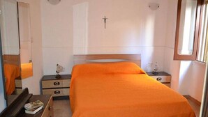 A bedroom with a bed, a dresser, a nightstand, a cross on the wall, and a window. - Three-room Holiday Home With Outdoor Space and a few Steps From the Cliff (Melendugno)