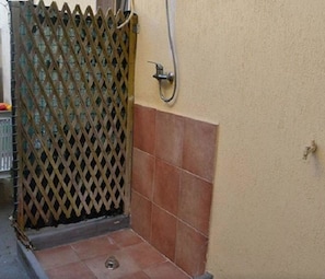 Een badkamer met een douche, betegelde vloer en een gesloten roede.