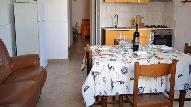 A dining area with a table set for two, a kitchen in the background, and a brown leather chair to the left. - Three-room Holiday Home With Outdoor Space and a few Steps From the Cliff (Melendugno)