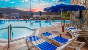 A pool area with lounge chairs and umbrellas, surrounded by stone walls and a view of mountains. - Spacious Apartment With Jacuzzi and Pool Access (Mogan)