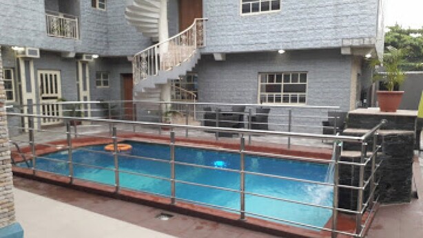 A swimming pool with a metal railing, a staircase, and a building with a gray facade. - Room-valley Front View Hotel- Guest Room (Lagos)