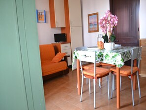 A dining area with a table set for four, a sofa, a television, and a door in the background. - Holiday Home With Balcony and air Conditioning in Torre Dell'o (Melendugno)