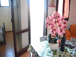 A dining area with a table set for two, a vase of pink orchids, and a bottle of wine.