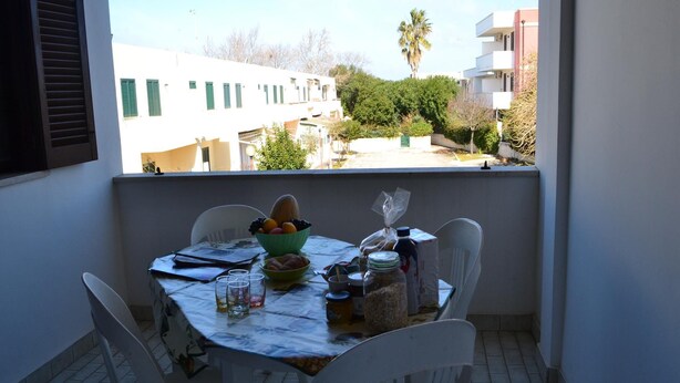 A balcony with a table set for dining, a bowl of fruit, and a view of buildings and trees. - Holiday Home With Balcony and air Conditioning in Torre Dell'o (Melendugno)