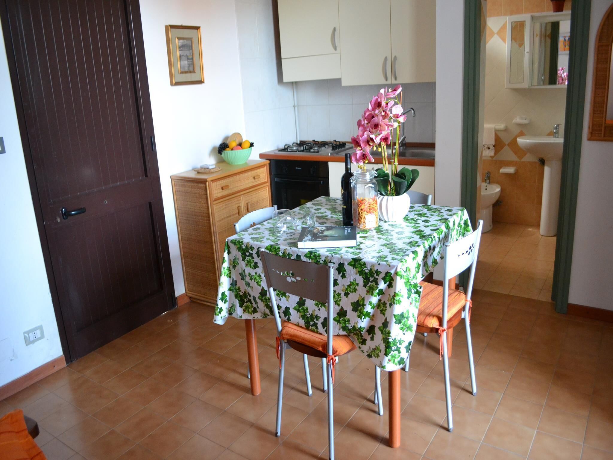 Un comedor con una mesa preparada para dos, una cocina al fondo y un baño visible a través de una puerta abierta.