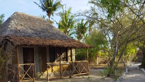 A rustic hut with a thatched roof, surrounded by sand and sparse vegetation. - Room-mida Creek Eco Camp 1 (Watamu)