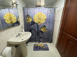 A bathroom with a sink, mirror, shower curtain with floral design, and a mat with a flower design. - Spacious 3-bedroom Apartment in Santo Domingo! (Santo Domingo Norte)