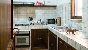 A compact kitchen with white tiled walls, a microwave, a gas stove, and wooden cabinets. - Split Level Aprtment (Rome)