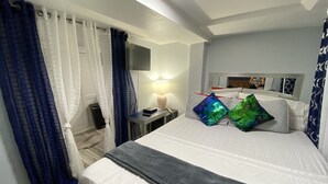 Una camera da letto con un letto, un comodino, una lampada, uno specchio e una finestra con tende.