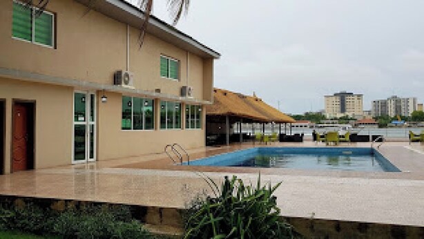 Un bâtiment doté d’une piscine, d’un espace couvert avec des chaises et d’un palmier.