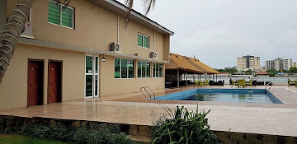 Un bĂątiment dotĂ© dâune piscine, dâun espace couvert avec des chaises et dâun palmier.