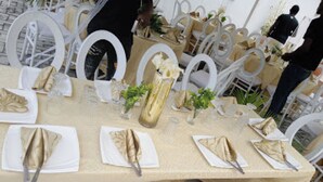Une table de banquet dressée avec des chaises blanches, des serviettes dorées et un vase doré.
