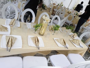Une table de banquet dressée avec des chaises blanches, des serviettes dorées et un vase doré.