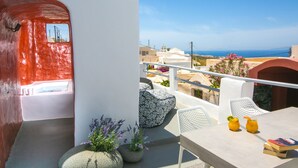 A balcony with a white railing, a table with two drinks and a book, and potted plants with purple flowers. - Executive Villa With Private Outdoor Plunge-pool, Sea Sunset View 4 Guests (Santorini)