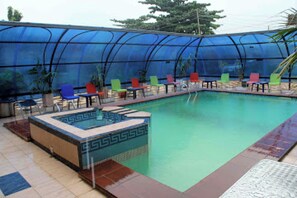 Una piscina con cerramiento de vidrio, rodeada de sillas y mesas coloridas.