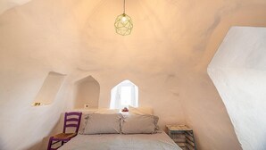 Ein gemütliches Schlafzimmer mit Bett, Stuhl, Pendelleuchte und Fenster.