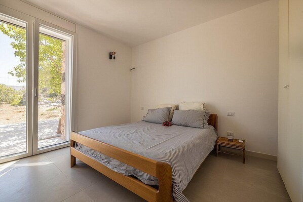A bedroom with a wooden bed, a small bedside table, and a large sliding glass door leading to an outdoor area.