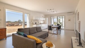 Ein modernes Wohnzimmer mit grauem Sofa, einem Essbereich mit Tisch und Stühlen sowie einer Küche im Hintergrund.