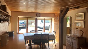 Un comedor con techo de madera, un reloj, piso de baldosas y vista a coches estacionados a través de puertas de vidrio.