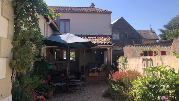 Un patio con zona de estar cubierta, rodeado de plantas y flores en macetas.