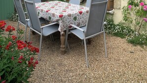 Un patio con mesa y sillas, rodeado de un jardín con flores y plantas.