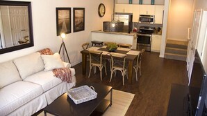 A compact living space with a sofa, dining table, chairs, a coffee table, a lamp, and a kitchen area with appliances.