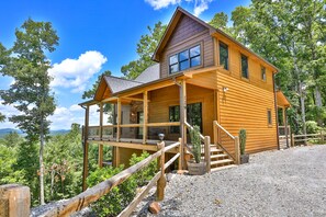 A wooden cabin with a porch, a staircase, and a view of the surrounding forest.
