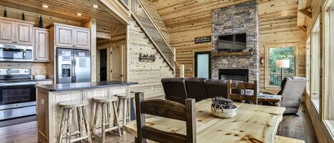 A spacious log cabin interior with a kitchen, dining area, and a fireplace.