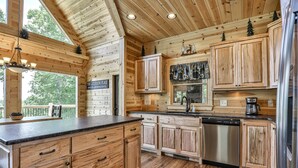 Une cuisine rustique, située dans une cabane en bois, avec un plan de travail en pierre, des placards en bois, un lave-vaisselle et une machine à café.