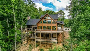 Une cabane en bois à deux étages, dotée d’un balcon et entourée d’une forêt dense.