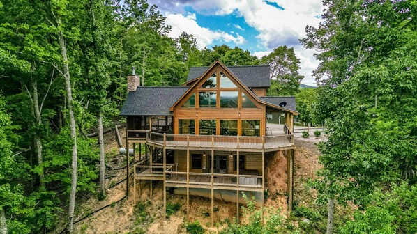 A two-story wooden cabin with a balcony, surrounded by dense forest.