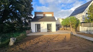A modern house with a large backyard, a wooden deck, and a fenced area.